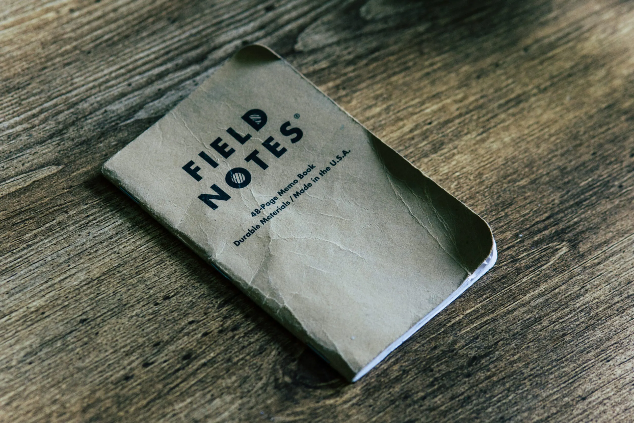 Field Notes notebook, wrinkled and worn, lays on a wooden tabletop. Photo by Kolby Milton on Unsplash.